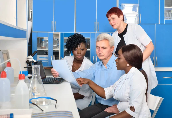 病院の検査室で科学者や医学の多文化チームは Covid 19コロナウイルス検査のためのテストシステムを議論します ヨーロッパのシニア同僚やジュニアアフリカの研究室のメンバーや学生 — ストック写真