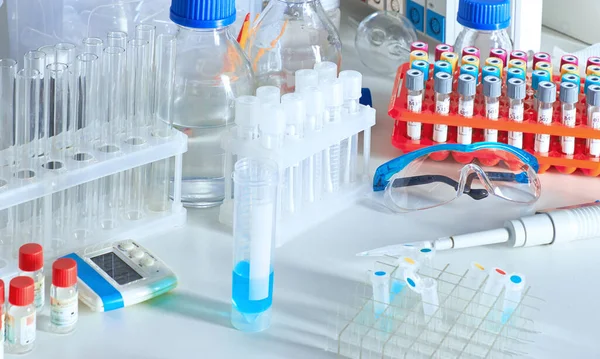 Scientific background with patient blood samples, reagents, chemicals, protective glasses, buffer solutions in glass bottles. Liquid scientific or medical samples in various glass and plastic tubes.