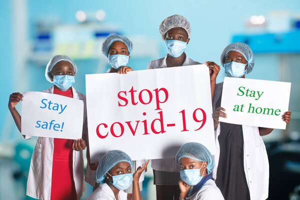 Group of African women nurses activists in face mask with hand sign placard with captions Stop Covid-19. Group of medics with message for public, information campain.