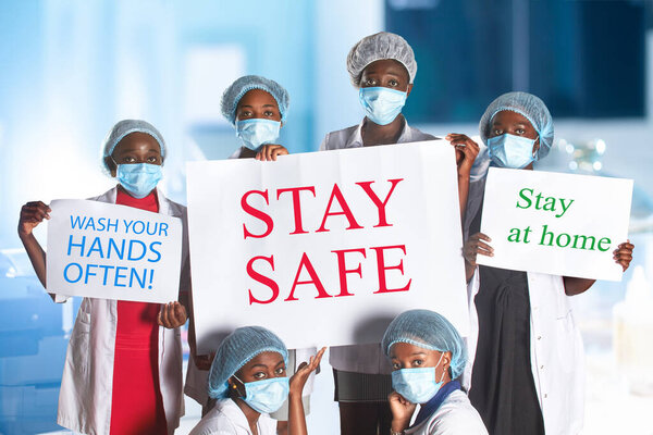 Group of African women nurses activists in face mask with hand sign placard with captions Stay at home, wash your hands. Group of medics with message for public, information campain.