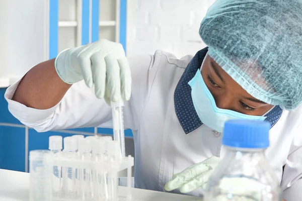 Afrikalı kadın teknisyen, teknik asistan, ağız örnekleriyle çalışıyor, Covid-19 'un tespiti için hasta örnekleri, SARS-CoV-2' nin yeni koronavirüsü. Test laboratuarında. Koruyucu giysi, maske, eldiven.
