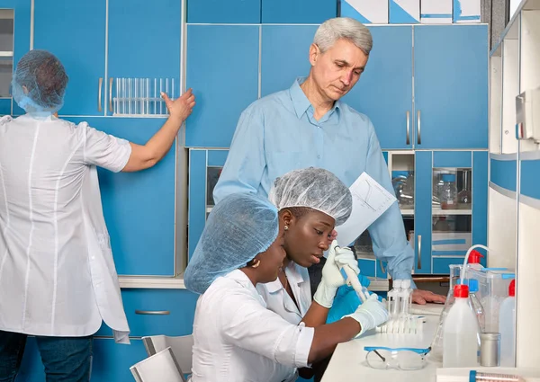新規のコロナウイルスに対する免疫を検出するためのCovid 19血液抗体検査の進捗報告 2人のアフリカの女医や学生は チームリーダー 白髪のヨーロッパのシニア男性にデータを示しています — ストック写真