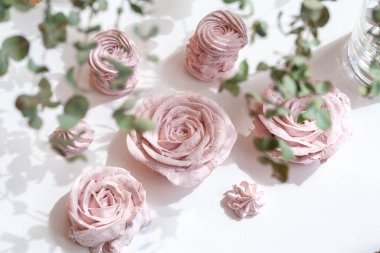 Güzel pembe dekoratif yenilebilir marshmallow gülleri, yaprakların arasından çekilen, bitkilerin ve çiçeklerin güzel gölgeleri, narin renkler, arka planın seçici bulanıklığı..