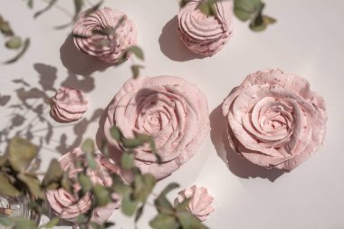 Güzel pembe dekoratif yenilebilir marshmallow gülleri, yaprakların arasından çekilen, bitkilerin ve çiçeklerin güzel gölgeleri, narin renkler, arka planın seçici bulanıklığı..