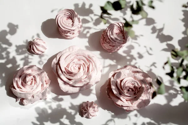 Güzel pembe dekoratif yenilebilir marshmallow gülleri, yaprakların arasından çekilen, bitkilerin ve çiçeklerin güzel gölgeleri, narin renkler, arka planın seçici bulanıklığı..