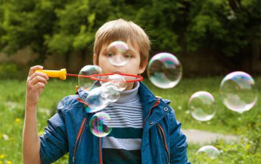 Küçük tatlı çocuk parkta sabun köpüklerini şişiriyor, çocukta neşeli duygular, parlak büyük sabun topları..