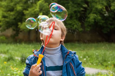 Küçük tatlı çocuk parkta sabun köpüklerini şişiriyor, çocukta neşeli duygular, parlak büyük sabun topları..