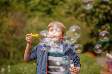 Küçük tatlı çocuk parkta sabun köpüklerini şişiriyor, çocukta neşeli duygular, parlak büyük sabun topları..