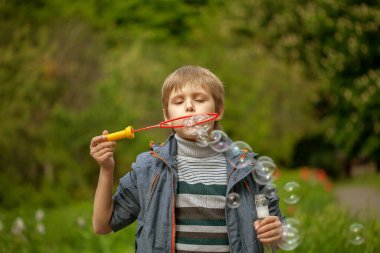 Küçük tatlı çocuk parkta sabun köpüklerini şişiriyor, çocukta neşeli duygular, parlak büyük sabun topları..