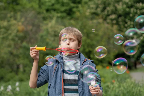 Küçük tatlı çocuk parkta sabun köpüklerini şişiriyor, çocukta neşeli duygular, parlak büyük sabun topları..