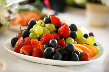 Böğürtlenli beyaz tabak Çilek, siyah üzüm, yeşil üzüm, masada elma. Sağlıklı bir yaşam tarzı. Meyve vitamini.