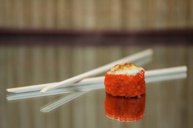 Suşi yuvarlanır ve ahşap bir arka plana yansıyarak yapışır..