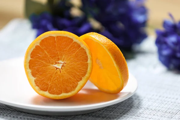 Orange on a white plate on a dark background with violet flowers