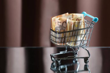 Paralı mavi alışveriş arabası. Yansıyan tablo. Karanlık arka plan. Mali işler. Finansal kriz. Bankacılık sistemi. Ekonomik bir sorun. Enflasyon. Para yazdırma.