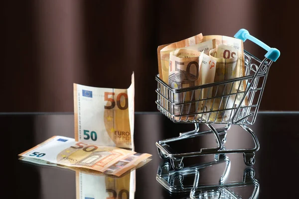 Paralı mavi alışveriş arabası. Yansıyan tablo. Karanlık arka plan. Mali işler. Finansal kriz. Bankacılık sistemi. Ekonomik bir sorun. Enflasyon. Para yazdırma.