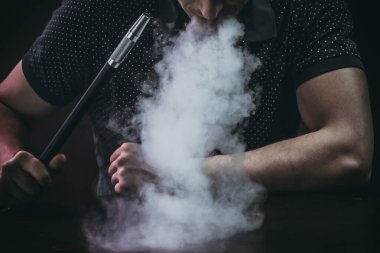 Erkekler siyah arka planda izole bir şekilde oturup nargile tüttürüyor.