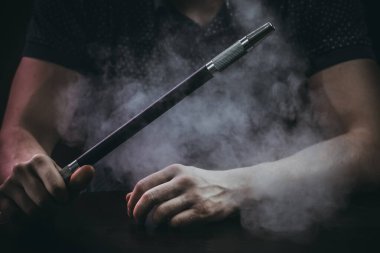 Erkekler siyah arka planda izole bir şekilde oturup nargile tüttürüyor.