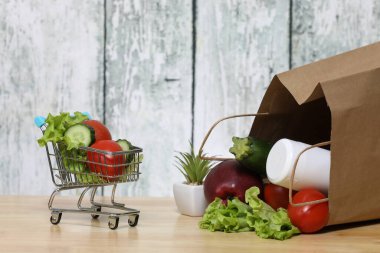 Alışveriş arabası ve bakkaliye. Ahşap arka planda sebzeli geri dönüşümlü kağıt alışveriş torbası. Eko ürün. Sebzeler. Salata.