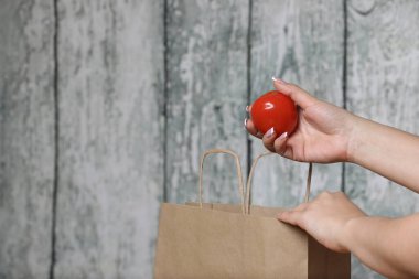 Ahşap arka planda geri dönüşümlü kağıt torbalı kırmızı domates tutan bir kadın.