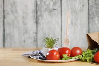 Yemek pişirmek için malzemeler. Tahta bir masada taze sebzeler. Domates ve salata. Ekoloji ürünleri. Kağıt torbayı geri dönüştür. Ahşap geri dönüşüm çatalı