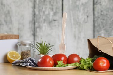 Yemek pişirmek için malzemeler. Tahta bir masada taze sebzeler. Domates ve salata. Ekoloji ürünleri. Kağıt torbayı geri dönüştür. Ahşap geri dönüşüm çatalı
