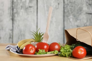 Yemek pişirmek için malzemeler. Tahta bir masada taze sebzeler. Domates ve salata. Ekoloji ürünleri. Kağıt torbayı geri dönüştür. Ahşap geri dönüşüm çatalı