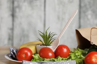 Yemek pişirmek için malzemeler. Tahta bir masada taze sebzeler. Domates ve salata. Ekoloji ürünleri. Kağıt torbayı geri dönüştür. Ahşap geri dönüşüm çatalı