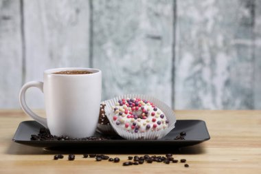 Beyaz kahve fincanı, üzerinde çikolata ve beyaz çikolatalı çörek olan ahşap bir masada. Sabah espresso. Sabah kapuçino bardağı.. 