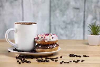 Beyaz kahve fincanı, üzerinde çikolata ve beyaz çikolatalı çörek olan ahşap bir masada. Sabah espresso. Sabah kapuçino bardağı.. 