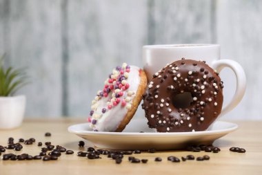 Beyaz kahve fincanı, üzerinde çikolata ve beyaz çikolatalı çörek olan ahşap bir masada. Sabah espresso. Sabah kapuçino bardağı.. 