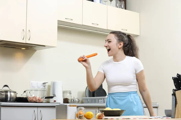 Young woman cooking in kitchen. Housewife preparing vegetables for cooking. Cooking soup. Singing in kitchen