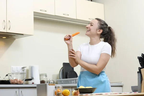 Young woman cooking in kitchen. Housewife preparing vegetables for cooking. Cooking soup. Singing in kitchen