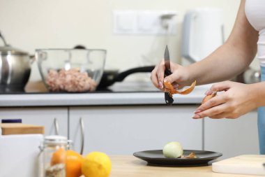 Mutfakta yemek yapan genç bir kadın. Ev hanımı yemek için sebze hazırlıyor. Soğan soy. Çorba yapıyorum.
