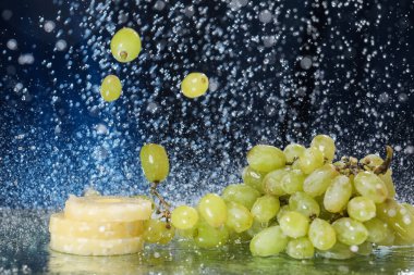 Suyun altında koyu mavi arkaplanda yeşil üzüm damlaları var. Sağlıklı bir yaşam tarzı. Multivitamin kokteyli. Yaz diyeti. Suyun altında meyve seti. Düşen üzüm ve ananas dilimleri