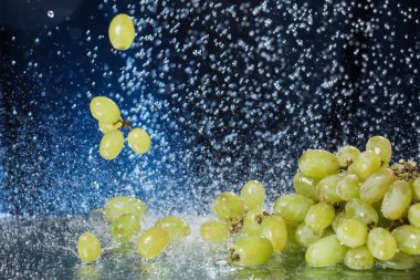 Suyun altında koyu mavi arkaplanda yeşil üzüm damlaları var. Sağlıklı bir yaşam tarzı. Multivitamin kokteyli. Yaz diyeti. Suyun altında meyve seti. Düşen üzüm dilimleri