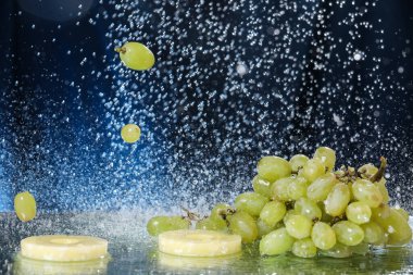 Suyun altında koyu mavi arkaplanda yeşil üzüm damlaları var. Sağlıklı bir yaşam tarzı. Multivitamin kokteyli. Yaz diyeti. Suyun altında meyve seti. Düşen üzüm ve ananas dilimleri