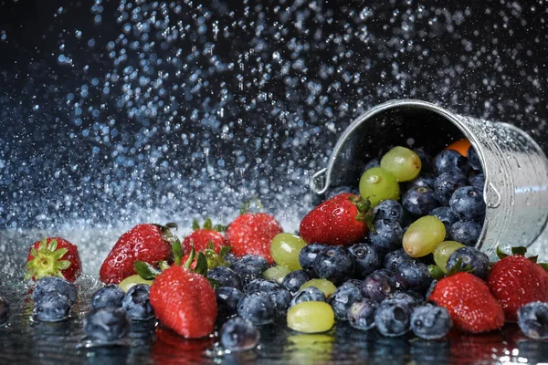 Meyve salatası düşen metal kovayla kapanır. Çilek, üzüm, yabanmersinli multivitamin kokteyli. Sağlıklı bir yaşam tarzı. Yaz diyeti. Su damlalarının altında meyve seti.