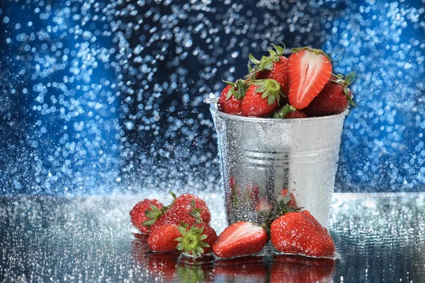 Çilekler metal bir kovanın içinde, suyun altında koyu mavi bir arka planda duruyor. Sağlıklı bir yaşam tarzı. Multivitamin kokteyli. Yaz diyeti. Suyun altında meyve seti.