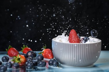 Süt damlaları, gri bir tabakta düşen böğürtlenleri kaplıyor. Yabanmersini ve çilekli multivitamin kokteyli. Sağlıklı beslenme. Organik yiyecekler. Siyah arkaplan.