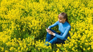 Cep telefonu sarı çiçekler çimenlerin üstünde tutan kadın.
