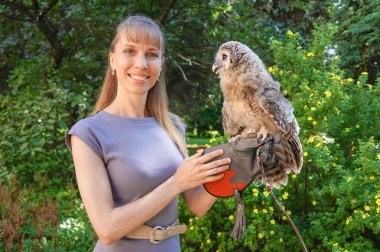 Çekici kadın kolunda bir baykuş ile gri elbiseli poz.