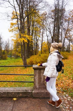 Parkta sonbahar manzara bakarak arka beyaz ceketli genç bayan. 