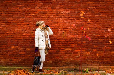 Bir cep telefonuyla konuşan beyaz elbise içinde Bayan düşmek vintage kırmızı tuğla duvar arka plan üzerinde.