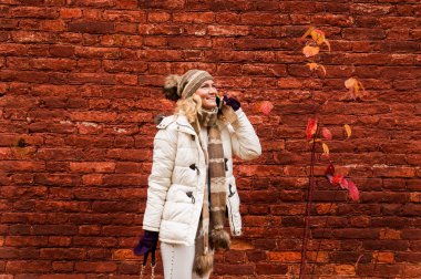 Bir cep telefonuyla konuşan beyaz elbise içinde Bayan düşmek vintage kırmızı tuğla duvar arka plan üzerinde.