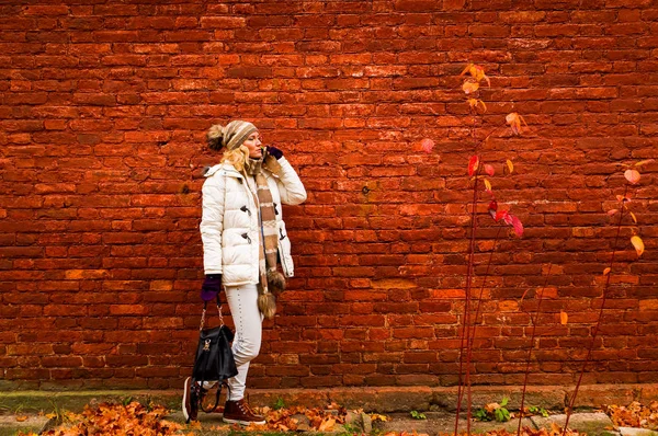 Bir cep telefonuyla konuşan beyaz elbise içinde Bayan düşmek vintage kırmızı tuğla duvar arka plan üzerinde.