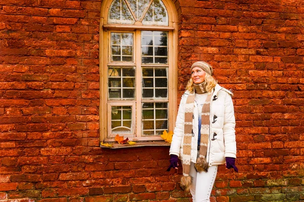 Bayan Beyaz giysili sonbahar vintage kırmızı tuğla duvar kemerli pencere ile bir arka plan üzerinde poz.