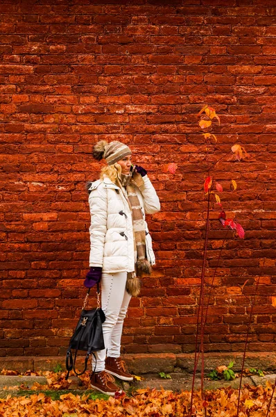 Bir cep telefonuyla konuşan beyaz elbise içinde Bayan düşmek vintage kırmızı tuğla duvar arka plan üzerinde.