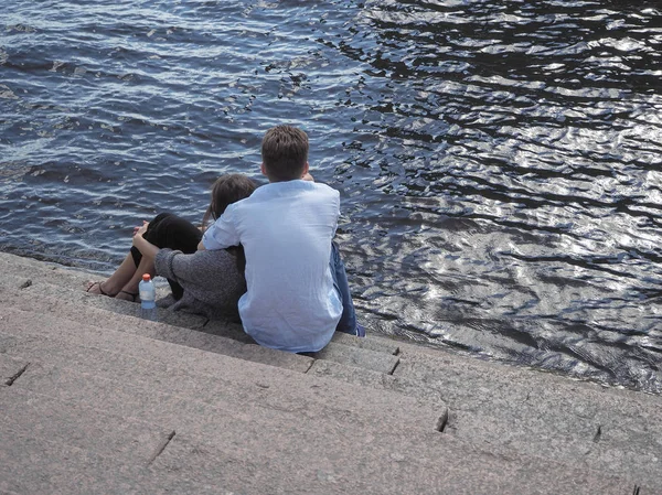 Loving couple resting in each other's arms sitting on the shore. Saint-Petersburg. The River Neva. — Stock Photo, Image