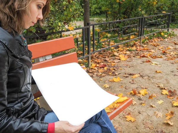 Woman in autumn Park leafing through the pages of the white album. Woman leafing through the pages. The woman on the bench in the fall.