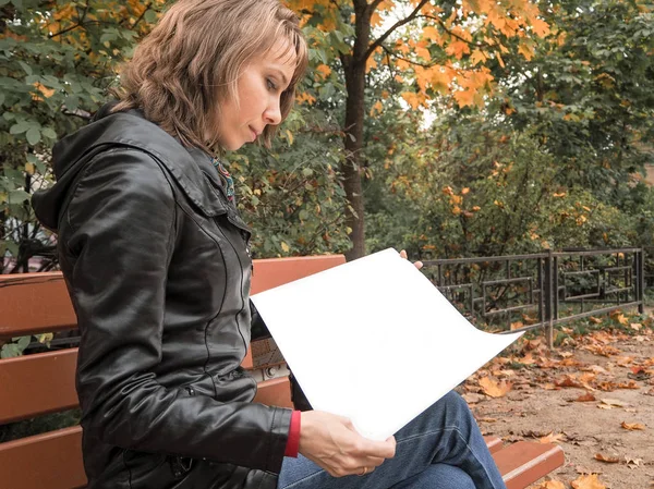 Mujer en otoño Park hojeando las páginas del álbum blanco. Mujer hojeando las páginas. La mujer en el banco en el otoño . — Foto de Stock